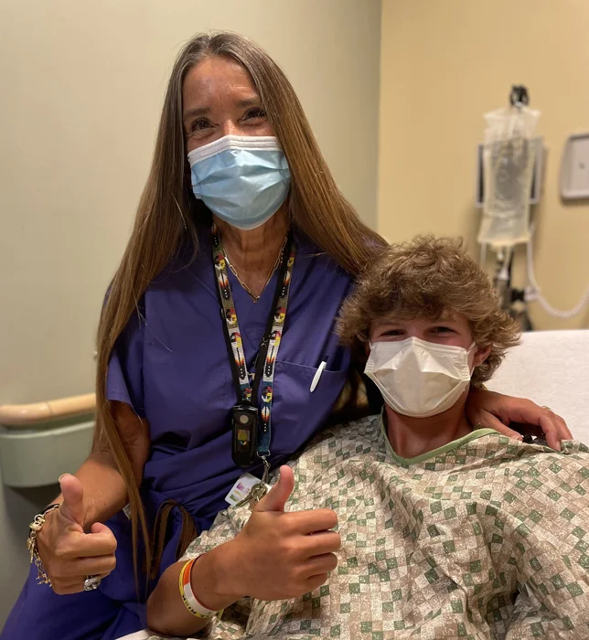 Pediatric Liaison Marilyn Richardson with boy in the pre-op room both with thumbs up while waiting for surgery