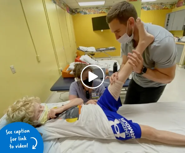 Two physical therapists holding up a young boy