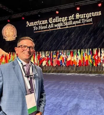 Dr. Bibbo on the stage with an American College of Surgeons sign and dozens of flags