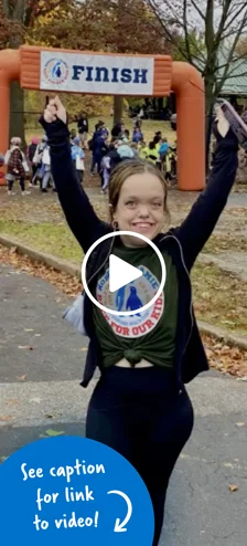 A young woman with her hands raised in celebration of reaching the finish line