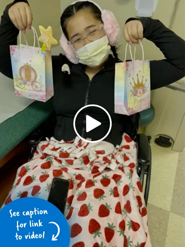 A young girl in a wheeelchair holding up two princess pamper goody bags