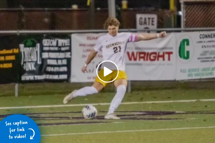 Teenage boy in a soccer uniform kicking a soccer ball on the field at a stadium