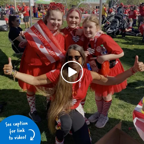 Photo of Pediatirc Liaison Marilyn Richardson kneeling with her thumbs up in front of three young female patients; they are all decked out in red clothing