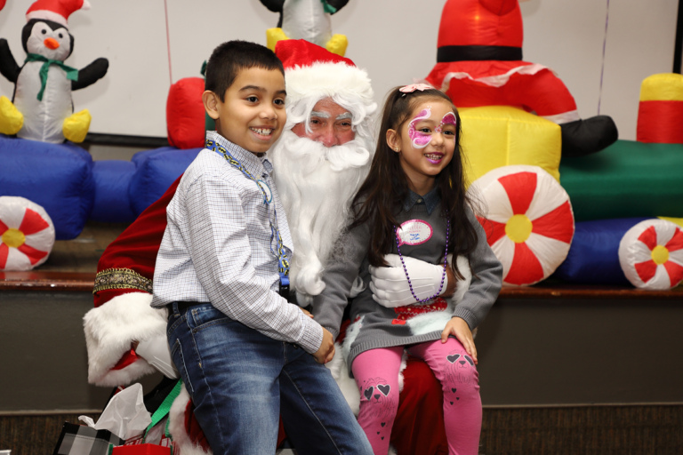 Girl with face painted and boy smiling sitting on Santa’s lap