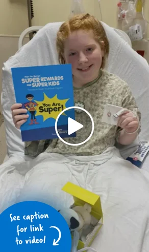 Young girl sitting up in a hospital bed holding a Super Rewards for Super Kids booklet and her Kendra Scott jewelry prize