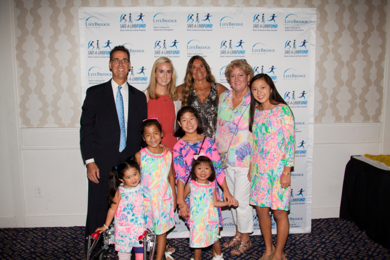 Pediatric Liaison Marilyn Richardson poses with family with 5 girls in matching pastel floral dresses at Rubin Institute for Advanced Orthopedics 2017 Save-A-Limb Fund Dinner