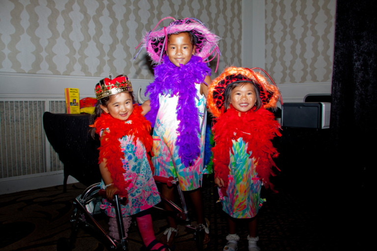3 young girls, one using a walker, dress up in bright boas and hats for the photo booth at Rubin Institute for Advanced Orthopedics 2017 Save-A-Limb Fund Dinner