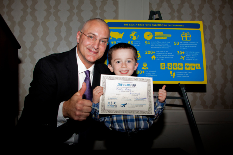 Dr. Shawn Standard and young boy with award both give a thumbs up at Rubin Institute for Advanced Orthopedics 2017 Save-A-Limb Fund Dinner