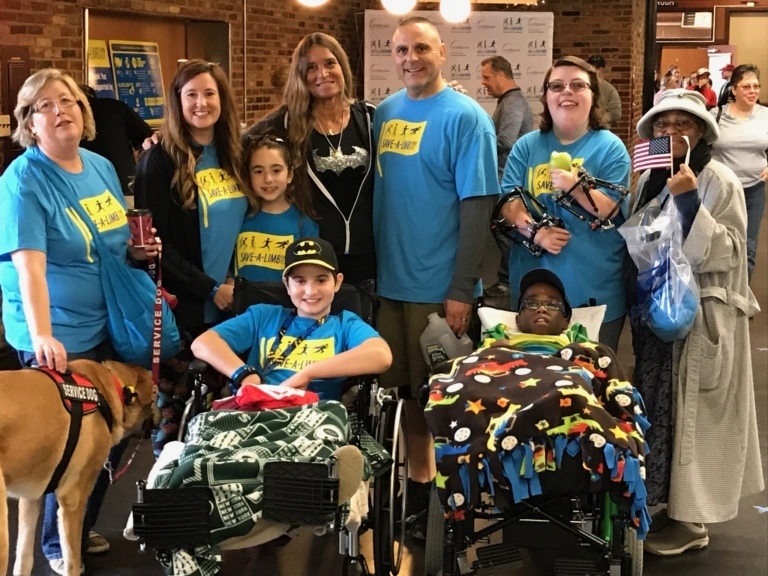 Pediatric Liaison Marilyn Richardson poses for a picture with parents, girl with 2 external fixators on her arms, 2 boys in wheelchairs, a young girl and a service dog at Rubin Institute for Advanced Orthopedics 2017 Save-A-Limb Fund Event