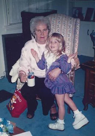 Carly at age 3 or 4 wearing a large shoe lift standing in front of her grandmother sitting in a chair