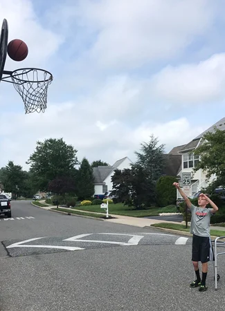 Jeffrey shooting a basket in a basketball hoop on the street with a walker behind him while being treated with a Precice internal nail and 8 plate