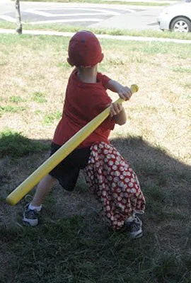 Jeffrey as a young boy wearing an external fixator with a cover from behind and batting playing wiffle ball in a yard