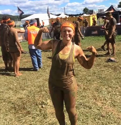 Carly wearing muddy clothes and showing off her muscles at Tough Mudder