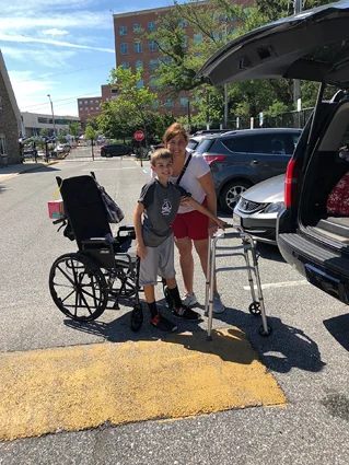 Preston and his mom with his wheelchair and walker in the parking lot at the Hackerman-Patz House