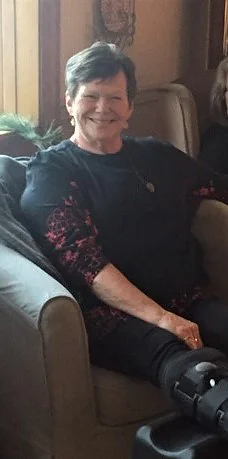 Sharon smiling while seated in a chair with an ankle boot on