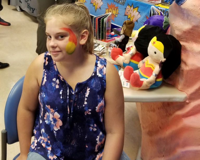 Girl Patient getting her face painted by a table of stuffed plush Wonder Woman toys