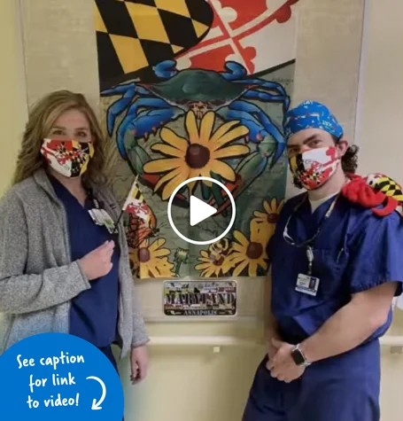 Renee Hunter and Dr. Philip McClure standing in front of a Maryland-themed banner and wearing Maryland-flag masks.