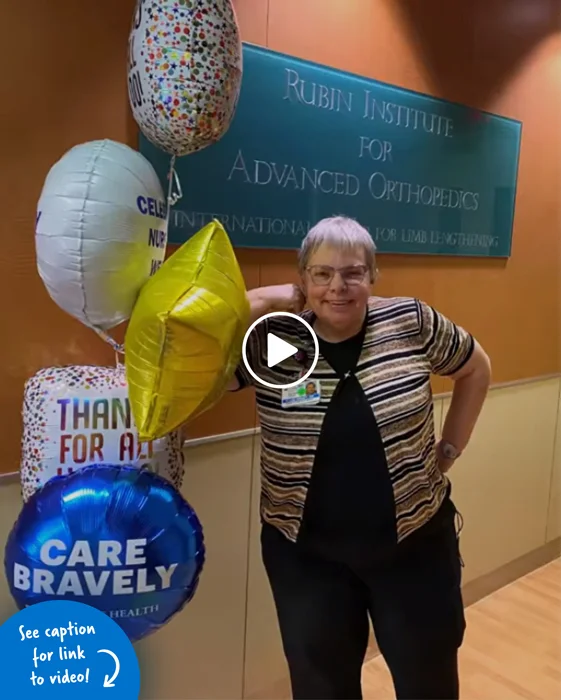 Lee Brady standing with balloons in front of a sign that reads Rubin Institute for Advanced Orthopedics, International Center for Limb Lengthening