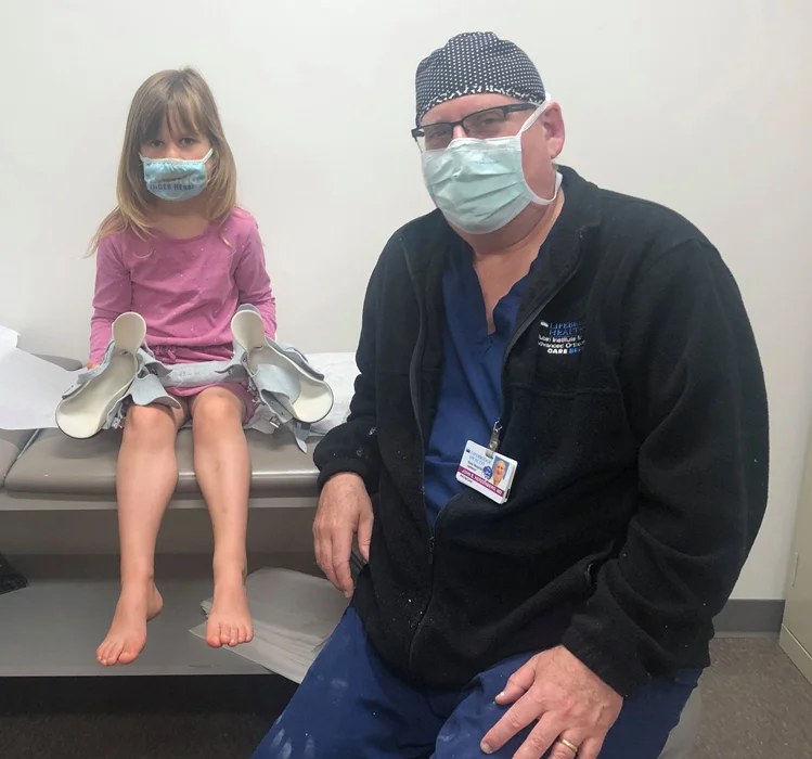 Dr. John Herzenberg with a girl holding her boots and bar from her treatment for clubfoot using the Ponseti Method