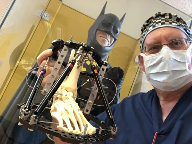 Dr. Herzenberg holding a model of a PonseTaylor frame in front of Batman