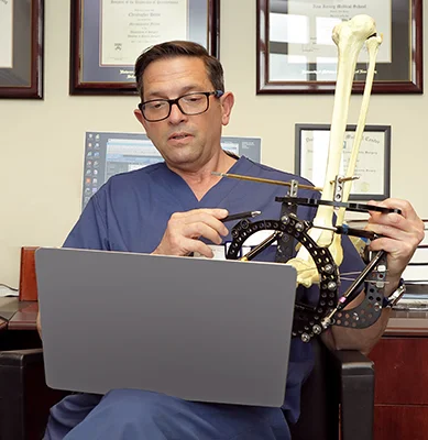 Dr. Christopher Bibbo holding a bone model in an external fixator while talking to a patient on a virtual doctor visit.