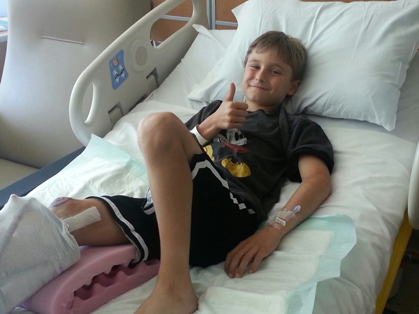 Josh as a boy in a hospital bed giving a thumbs up sign