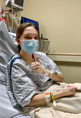 Lexie giving the thumbs up signal in her hospital bed before surgery